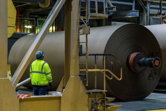 An IP employee surveys a large roll of brown paper coming off the assembly line